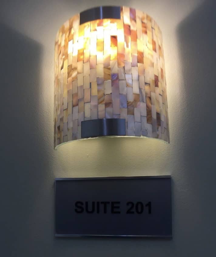 A wall-mounted mosaic light fixture glows above a sign that reads "SUITE 201" in bold black letters on a metallic background.